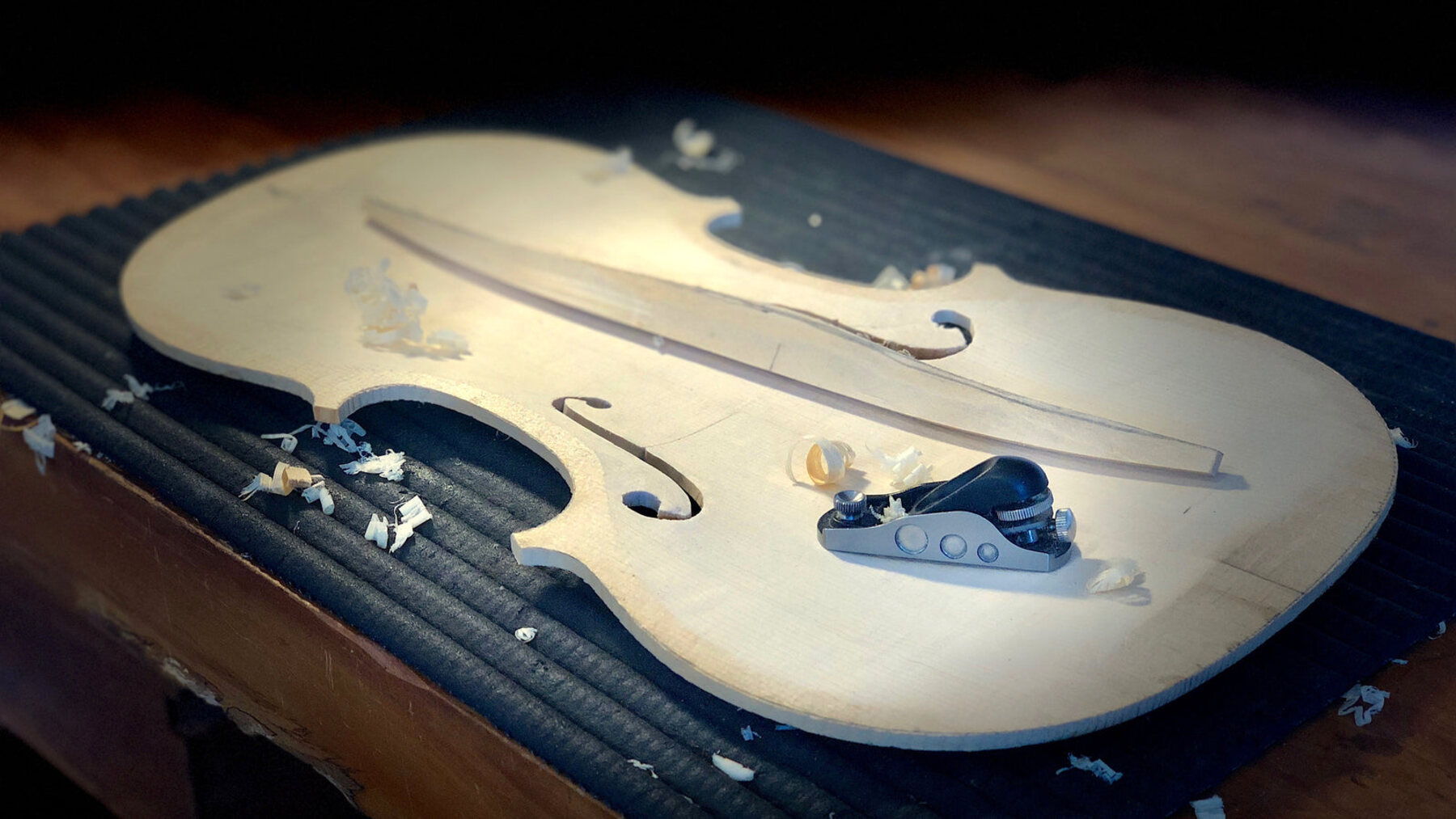 Tampo de violino em spruce sendo entalhado à mão sob luz dramática